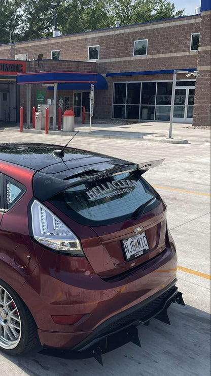 Red car with a black roof and spoiler parked in front of a gas station.